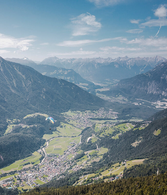 Eine malerische Luftaufnahme, umgeben von üppig grünen Wäldern und hohen Bergen unter einem teilweise bewölkten blauen Himmel.