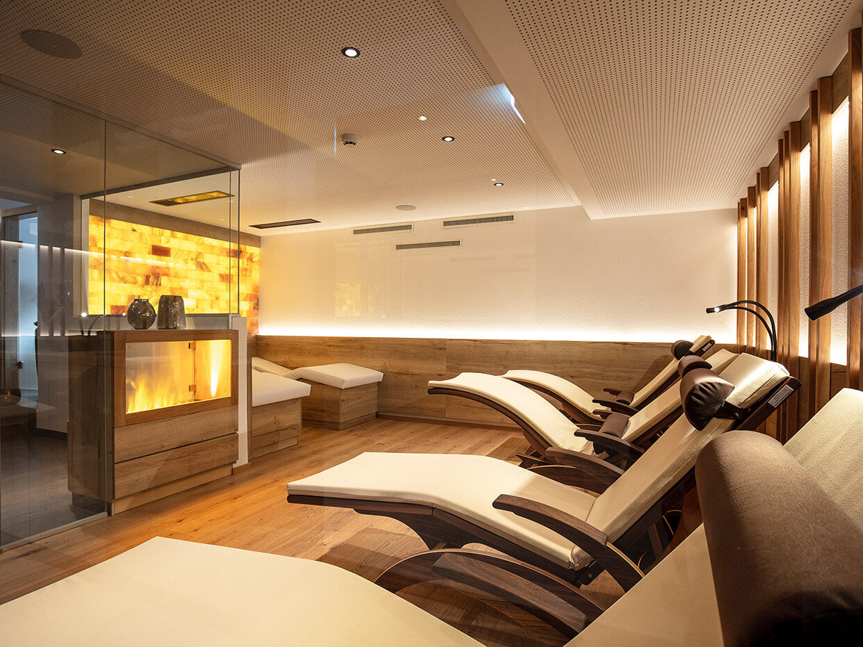 Ein moderner Ruheraum mit mehreren geschwungenen Liegestühlen, sanfter Beleuchtung, Holzakzenten und einer leuchtenden Wand, die eine ruhige, Spa-ähnliche Atmosphäre schafft.