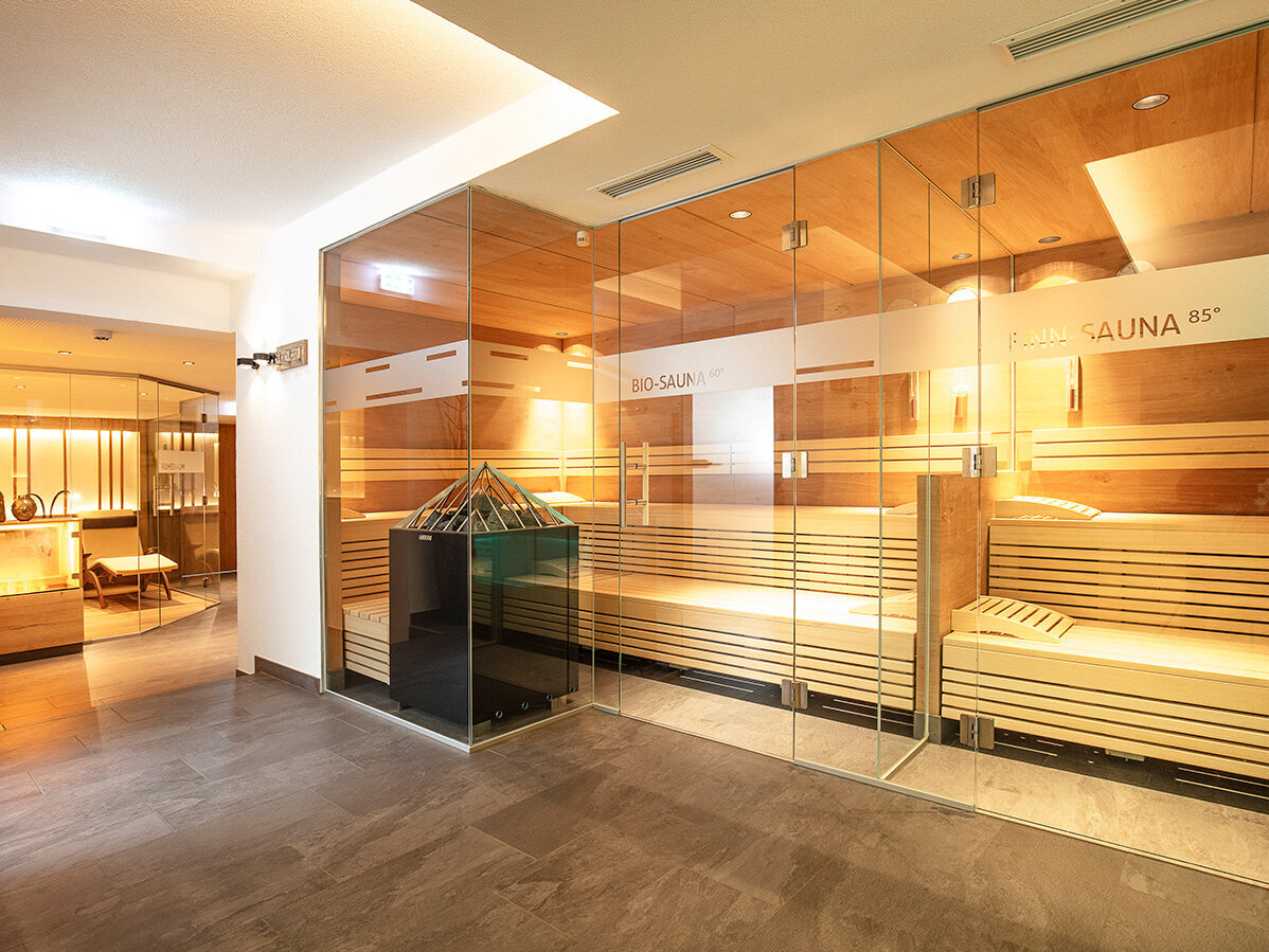 Modernes Spa-Interieur mit einer Sauna mit Glaswänden auf der rechten Seite, Holzbänken im Inneren und einem gemütlichen Ruheraum mit warmer Beleuchtung.
