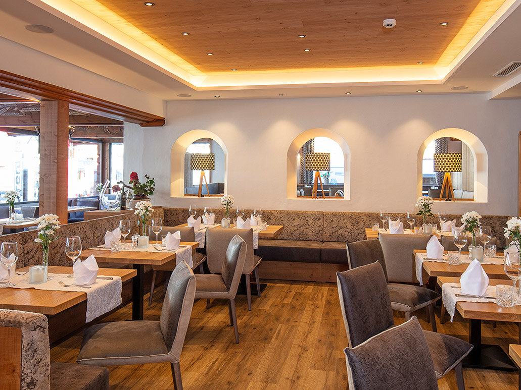 Elegantes Restaurantinterieur mit Holzböden, moderner Beleuchtung, gedeckten Tischen mit weißen Servietten, grauen Stühlen, Blumengestecken und dekorativen Nischen in der Wand.