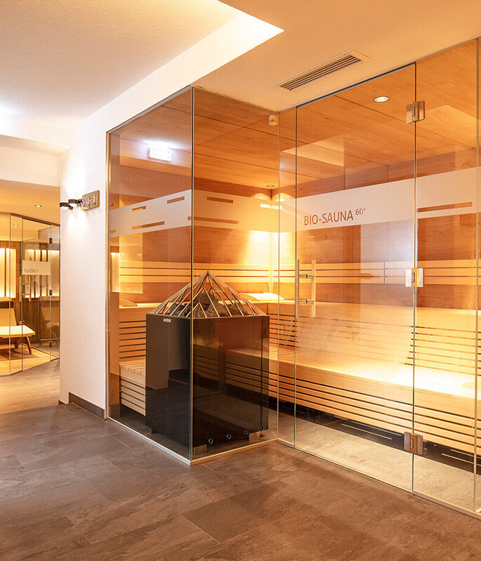 Moderne Spa-Innenausstattung mit verglasten Saunen, warmen Holzbänken, sanfter Beleuchtung und Zierpflanzen im Flur, die eine entspannende und einladende Atmosphäre schaffen.