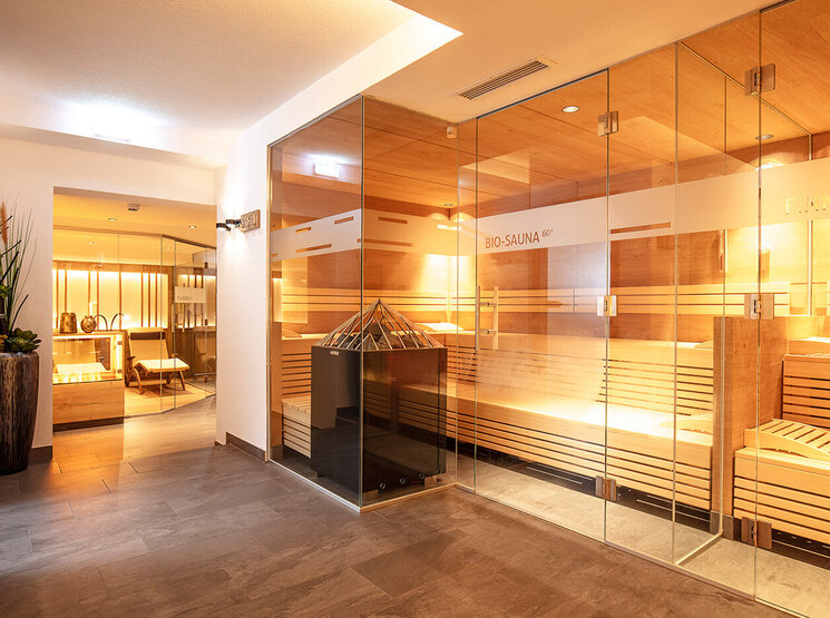 Moderne Spa-Innenausstattung mit verglasten Saunen, warmen Holzbänken, sanfter Beleuchtung und Zierpflanzen im Flur, die eine entspannende und einladende Atmosphäre schaffen.