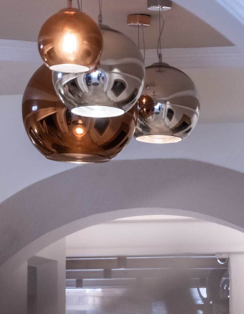 Kugelförmige Pendelleuchten aus Metall – zwei silberne und zwei kupferfarbene – hängen an der Decke über einem gewölbten Türbogen in einem modernen Innenraum.