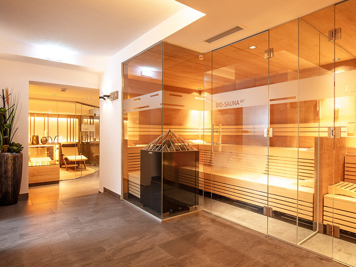 Ein modernes Spa mit glaswandigen Saunen, Holzbänken, einer Zierpflanze und eleganter Beleuchtung, die eine warme, entspannende Atmosphäre schaffen.