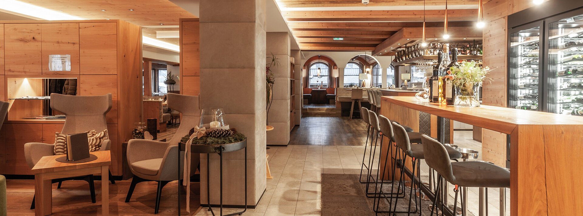 Ein modernes Restaurant mit Holzakzenten, gepolsterten Stühlen, einer Bar mit Barhockern, ausgestellten Weinflaschen und sanfter Beleuchtung, die eine warme und einladende Atmosphäre schafft.