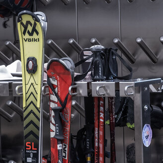 Eine Nahaufnahme eines Skiraums, in dem Skier, Stöcke, Schuhe und sonstige Ausrüstung auf Metallregalen an einer Wand mit schräg angeordneten Haken verstaut sind.