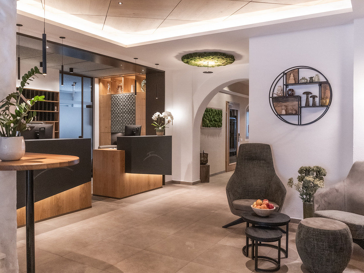 Moderne Hotellobby mit einer Rezeption, stilvollen Stühlen, einem kleinen Tisch mit Obst, dekorativen Regalen, Pflanzen und warmer Beleuchtung, die eine einladende und gemütliche Atmosphäre schaffen.